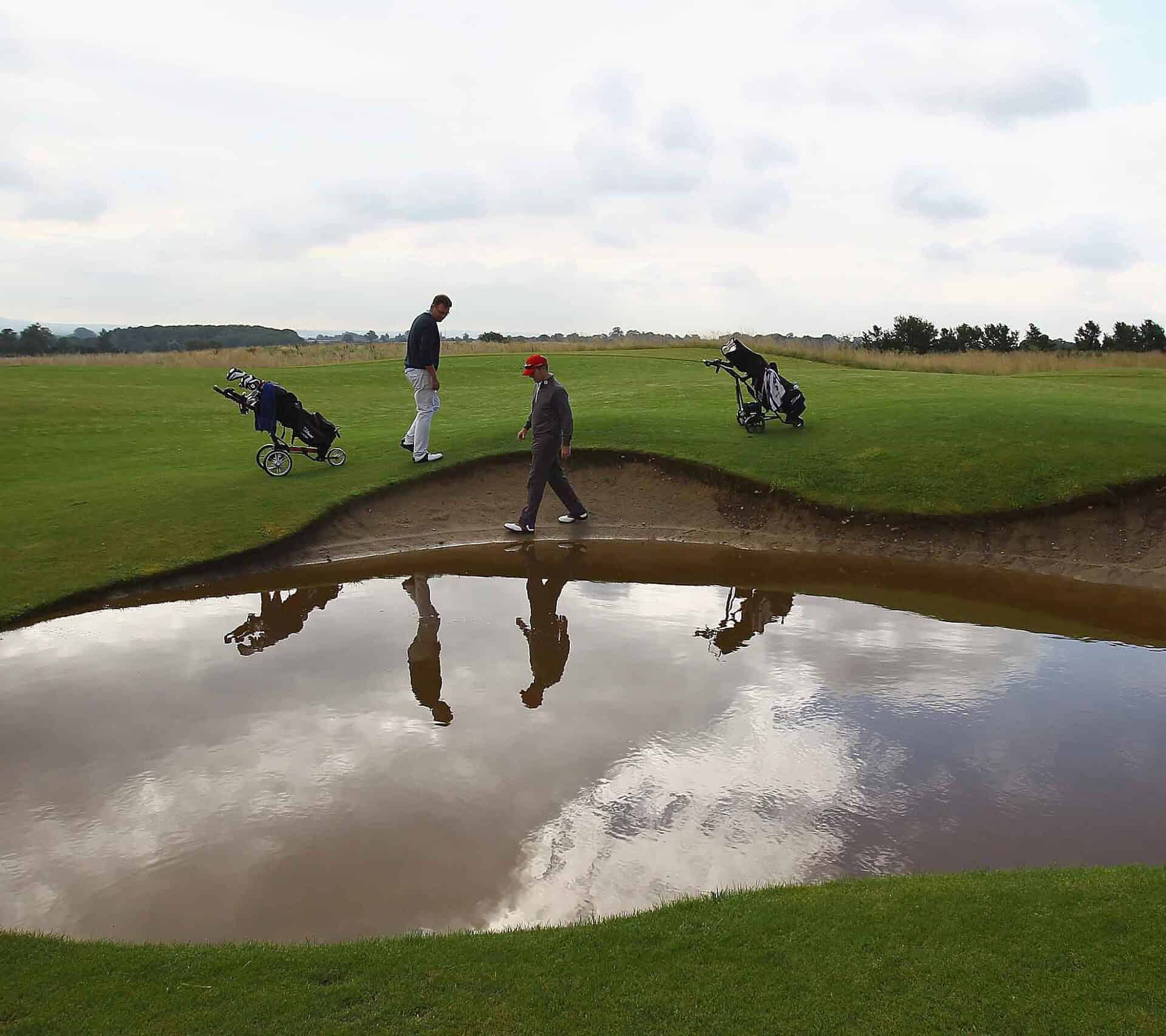 John Jacobs (L) of Cumberwell Park Golf Club looks for his ball in a flooded bunker with Richard Dinsdale of Parc Golf Academy during the Lombard Challenge Regional Qualifier at Cumberwell Park Golf Club on August 6, 2012 in Bath, England | Source: Getty Images